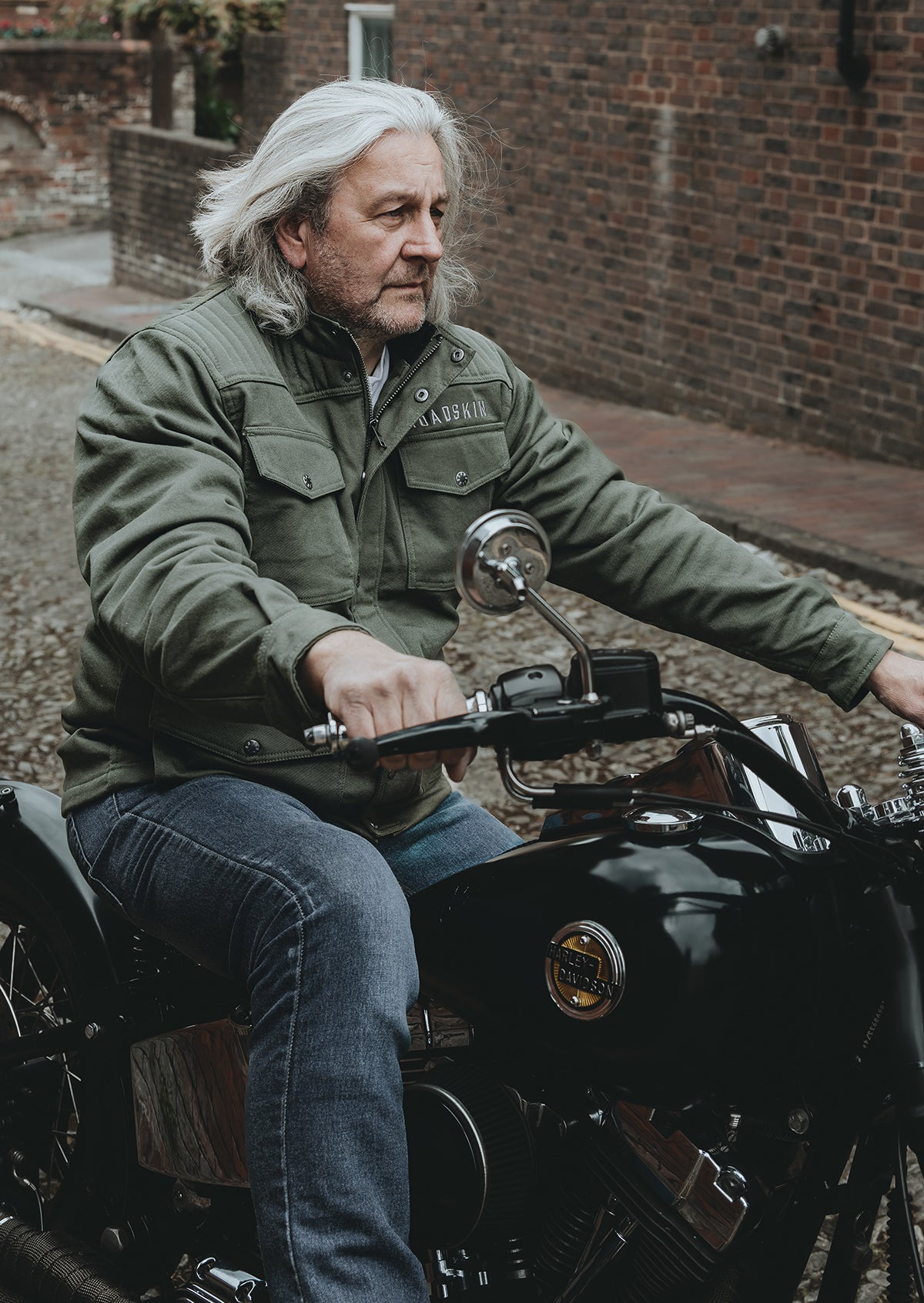 Man sitting on a motorcycle wearing a green jacket in an urban setting.