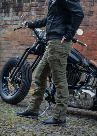 Lady standing next to a motorcycle wearing olive coloured motorcycle trousers.